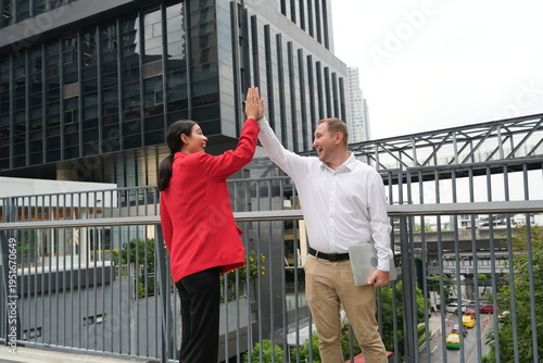 A female staff member and a male employee walk to work carrying tablets and meet outside the company in the morning, greeting each other.
