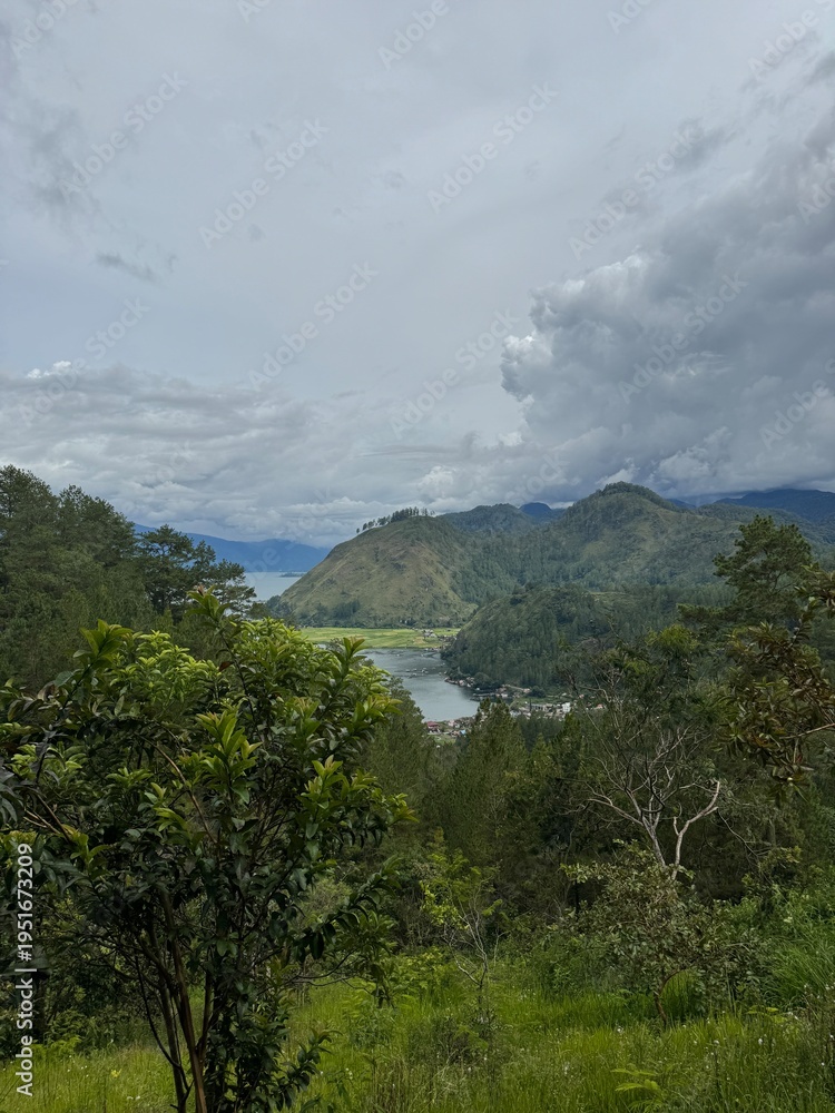 Fototapeta premium Scenic view of a mountain valley with a lake surrounded by green forest under a dramatic cloudy sky. Represents nature, travel, and outdoor landscape beauty.