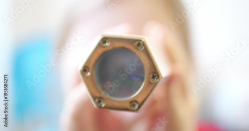 High Key Shot of Young Child Looking into Handmade Kaleidoscope with Brushed Brass Metal Front Plate Matte Glass and Eight Screws creating Unique Geometric Patterns from Colorful Glass fragments