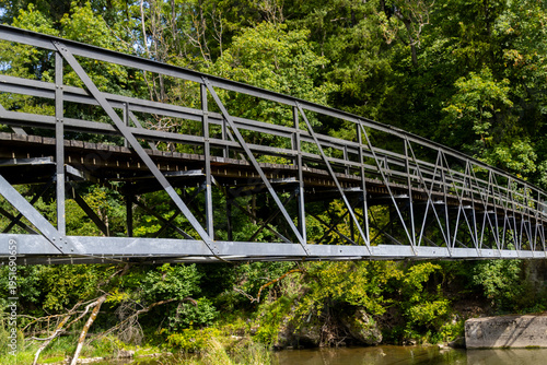 Historic Iron Truss Footbridge Spanning River Through Lush Green Forest Landscape