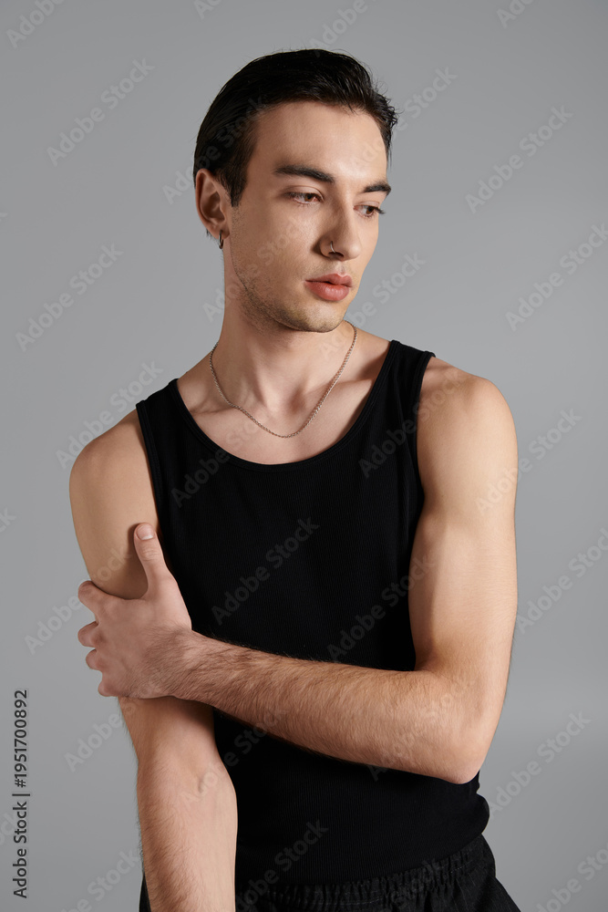 Fototapeta premium Young man showcases modern fashion in black tank top against grey background