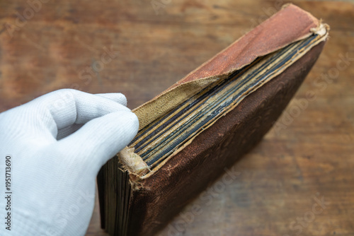 Restoration of an old book in the workshop.A hand in a white silk glove repairs the hardcover of a photo album.Preservation of ancient manuscripts and texts.The profession of a renovator.