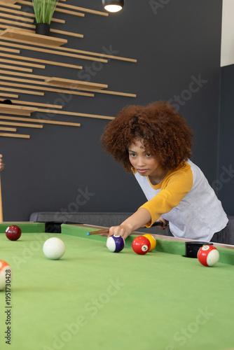 Teen friends playing on green pool table in game room, wearing raglan, aiming cue, copy space