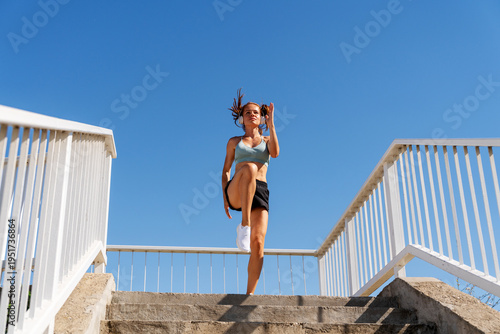 Fit woman performing High-Intensity Interval Training (HIIT) outdoors on urban steps in summer.