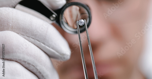 Caucasian male jeweler inspecting diamond with loupe and tweezers in workshop