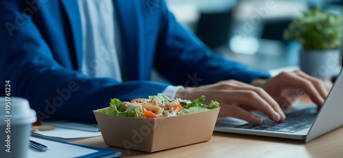 Employee enjoying healthy office lunch from takeaway box. Businessman working at desk with fresh salad meal in sustainable paper lunchbox