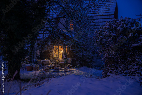 Night winter scene of a snowed in house with a bright warm light shining inside