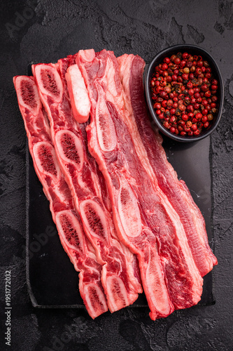 Tableau sur toile Premium raw short ribs (Kalbi style) and a meat fork on a black slate/stone surface, emphasizing quality and tools