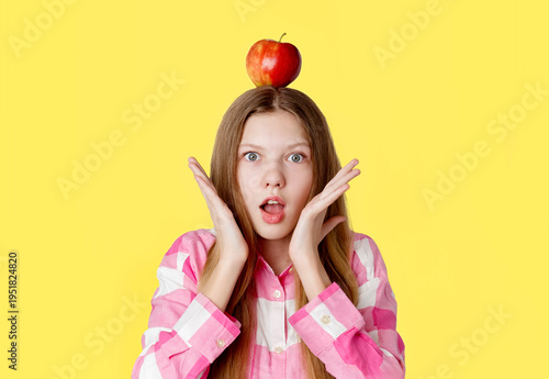portrait of a young happy girl with an apple on her head, emotion of surprise from an idea