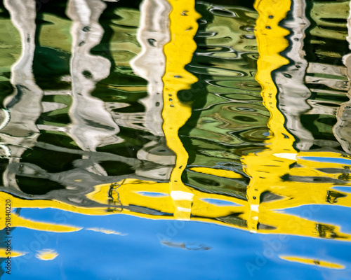 A soft‑focused view of a wharf reflects gently across the ocean’s surface, blending muted blue, yellow, green, and gray tones into a calm, painterly scene.