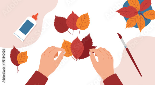 Hands carefully arranging colorful autumn leaves for a craft project with glue and a paintbrush on a white workspace surface.