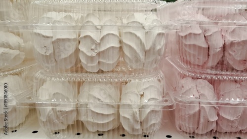 White and pink zephyr marshmallows packed in transparent plastic containers on store shelf. Soft textures of sweet confectionery. Rows of traditional Russian zephyr treats in blisters at supermarket