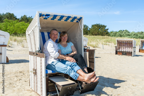 Happy middle aged couple sitting in traditional beach traditional windbreaks at Baltic Sea Germany enjoying summer vacation relaxation and travel lifestyle by sea