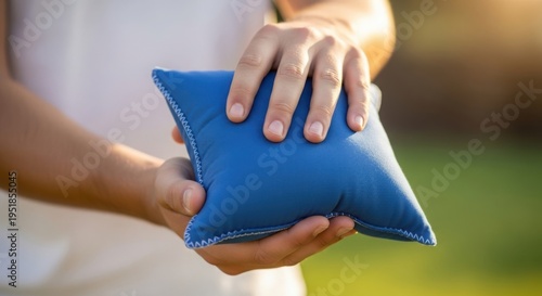 Person holding blue cornhole bean bag with focus on hands preparing for shot in outdoor setting, cornhole gameplay emphasized for social gatherings and casual competitions.