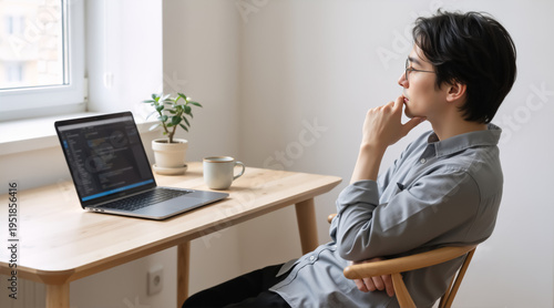 Asian software developer with glasses thinking at desk. Programmer looking at code on laptop screen. Web development