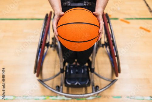 Person in a sports wheelchair ready for a game, holding a basketball on a gym court. Representing adaptive sports and inclusion