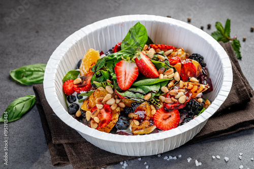 Fresh fruit salad with nuts and greens. A bowl contains a mix of fruit, nuts, and greens on a table with simple dark cloth.