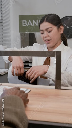 Vertical shot of African American man explaining request to teller, gesturing toward documents at counter