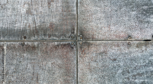 Close‑up of weathered concrete panels joined by metal bolts, showing rough gray texture, rust marks, and intersecting seams that create an industrial, worn surface pattern.