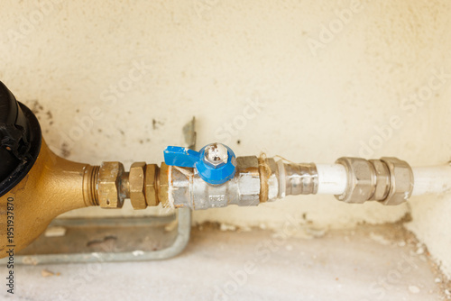 A close-up view of a manual shut-off ball valve with a blue handle connected to a household water meter system. Stock photo