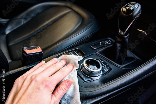 Close-up of male hand wiping car dashboard with microfiber cloth for cleaning. Concept of vehicle hygiene, interior maintenance and car detailing.