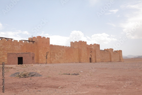 Desert Fortress Set at Atlas Studios in Ouarzazate.
A wide-angle view of a large fortress-like structure standing in the middle of a dry, open desert landscape. The sandy-colored walls, t