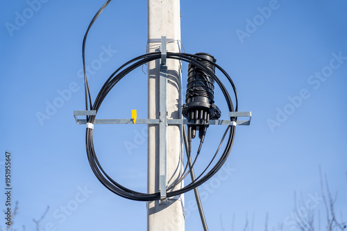 Принти на полотні Modern fiber optic network infrastructure: black splice closure with coiled cables mounted on concrete utility pole against vibrant blue sky, symbolizing high-speed internet connectivity