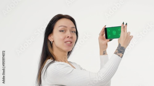 Adult young woman holds a phone with a green screen and smiles white background isolated space