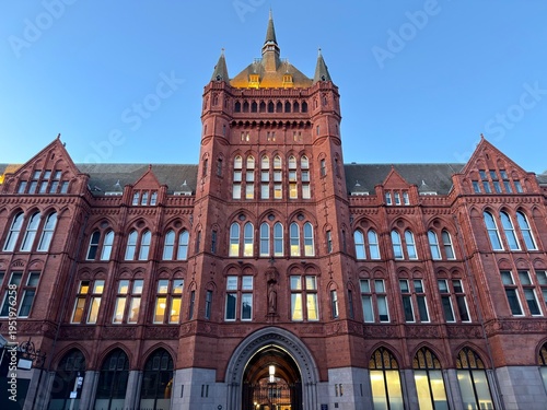 Foto [Intimidating Medieval Brick Grandeur]: A grand, regal, and multi-story red brick building with complex medieval inspiration and thousands of windows, dominating a European street