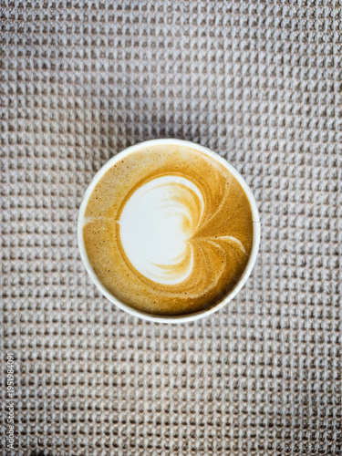 A white cup of freshly made coffee with milk on the gray table cloth with a grey textured tablecloth in the background. Minimalist concept, Thai