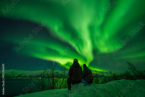 Couple watching bright Aurora Borealis over snowy mountains in Tromso