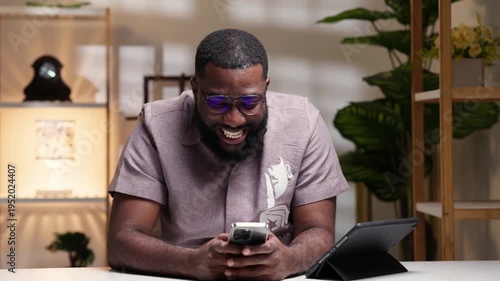 Cheerful young African man celebrating while looking at smartphone, enjoying a win or victory