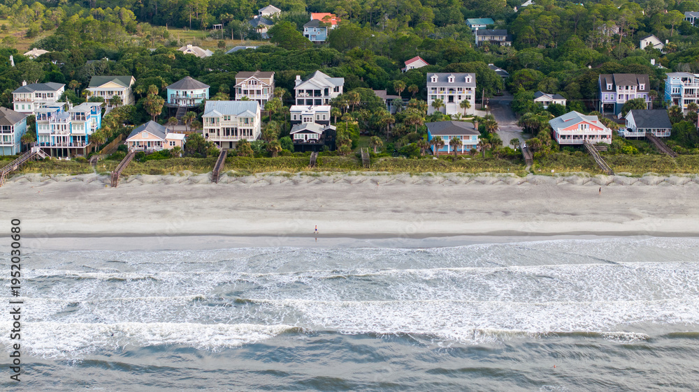 Obraz premium Aerial view of waterfront mansion homes in Folly Beach near Charleston, South Carolina landscapes with person runnning along beach and waves during morning light