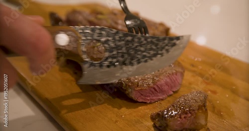 Closeup on sharp knife cutting rare stake on wood board - handheld shot