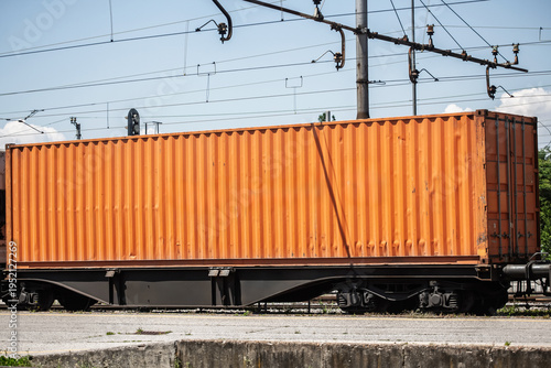 Orange shipping container mounted on a freight rail wagon. The image illustrates rail cargo handling, containerized freight and multimodal transportation within a logistics network.