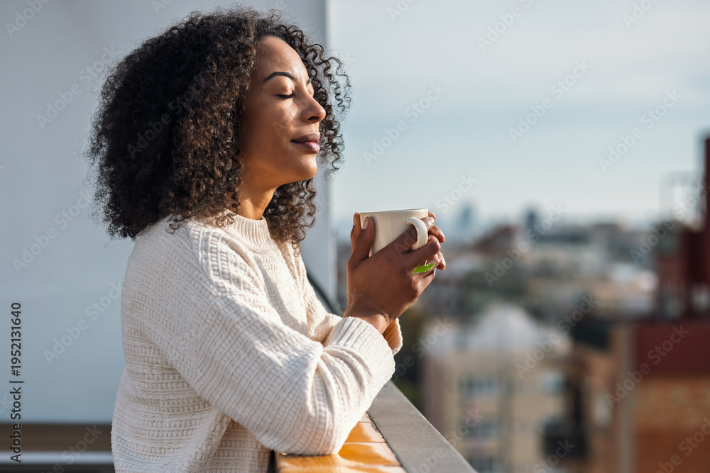Fototapeta premium Beautiful woman drinking a cup of tea while relaxing on her balcony at home