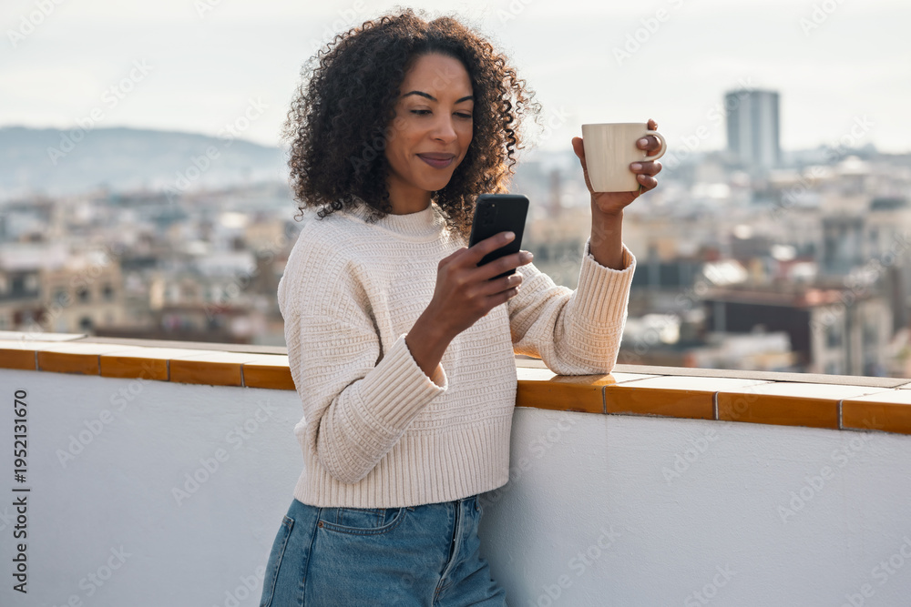 Fototapeta premium Beautiful woman drinking a cup of tea while doing a videocall on her balcony at home