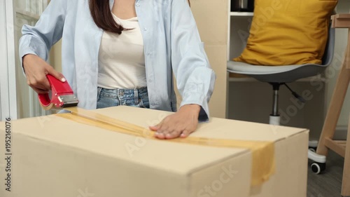Small business warehouse scene of worker apply shipping label on parcel and taping cardboard box, organizing delivery tasks, order preparation and maintaining efficient packing workflow, multitasking