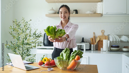 Smiling female nutritionist holding fresh organic lettuce in a bright kitchen. Healthy eating, diet planning, and clean lifestyle concept