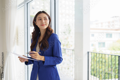 Confident businesswoman holding documents while standing by a large office window. Concept of business planning, management, and decision making concept. Free Download Confident businesswoman holding documents while standing by a large office window. Concept of business planning, management, and decision making concept. - GFXLoad