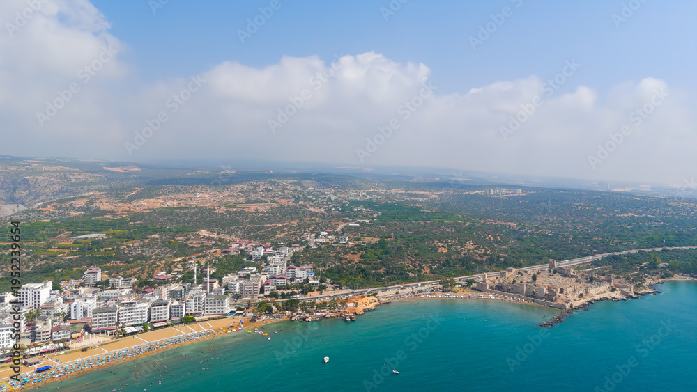 Fototapeta premium Kizkalesi, Mersin, Turkey. Breathtaking panoramic drone view from Maiden Castle island showing surrounding sea, city beaches and majestic Taurus mountains.. Aerial View