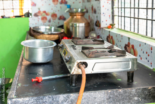 A rural Indian woman cooking on an LPG gas stove in a simple kitchen. The image highlights rising cooking gas prices, energy crisis,