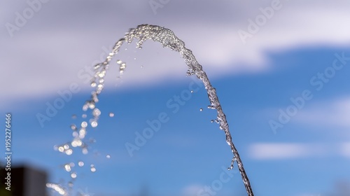 parabola. A single jet of water arches gracefully from a fountain against a bright sky. travel magazines, destination branding, designed for outdoor magazines and nature guides.