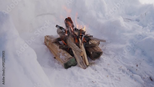 Wallpaper Mural Small campfire made of stacked firewood burning inside a snow pit in winter. Orange flames flicker between wooden logs while the fire burns in cold outdoor conditions. High quality 4k footage Torontodigital.ca