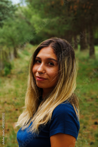 portrait of a young Latino brunette girl using Jeans and a blue shirt in a country setting with a lot of green and trees in the background