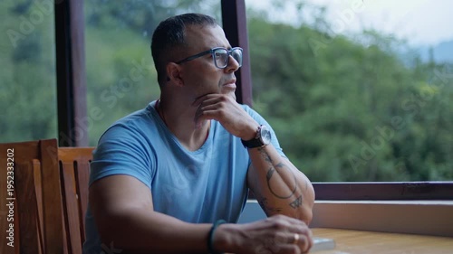 Man spending leisure time in countryside café, sitting quietly and thinking while enjoying outdoor scenery.