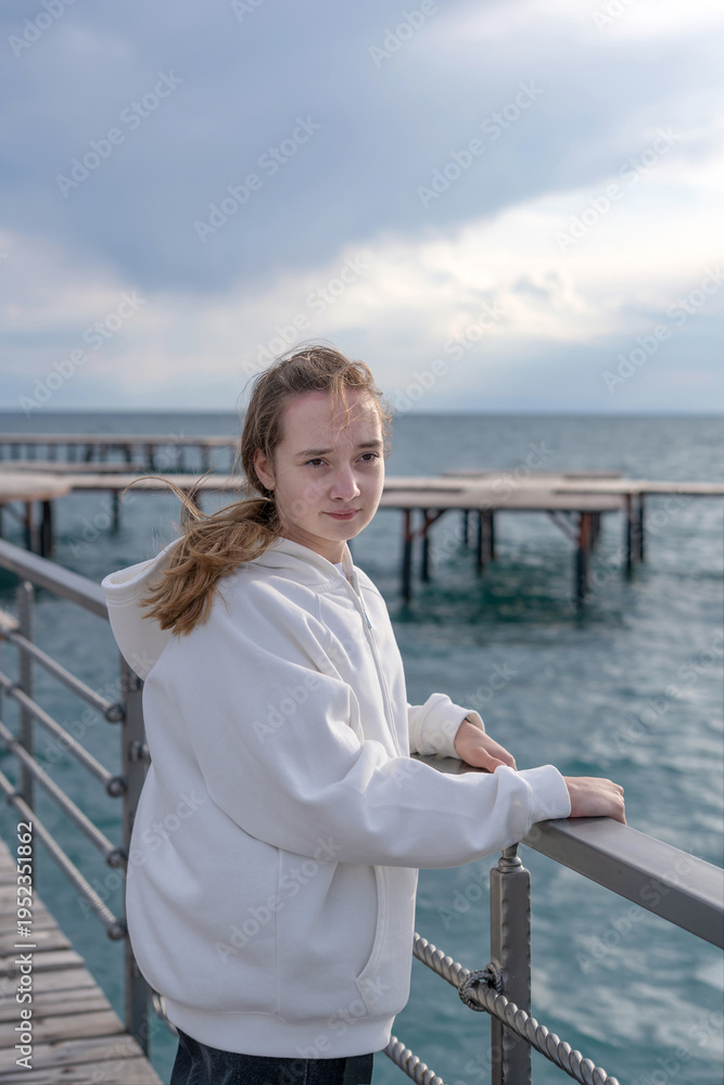 Fototapeta premium A teenage girl walks along the beach and pier at sunset on Lake Issyk-Kul. Concept: Family vacation trip