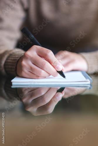 Vertical closeup image of a woman writing on a notebook on the table