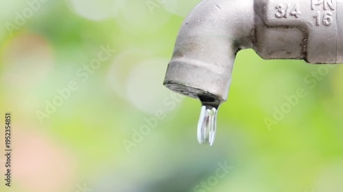 A close-up of a dripping faucet with a soft green background, symbolizing water conservation