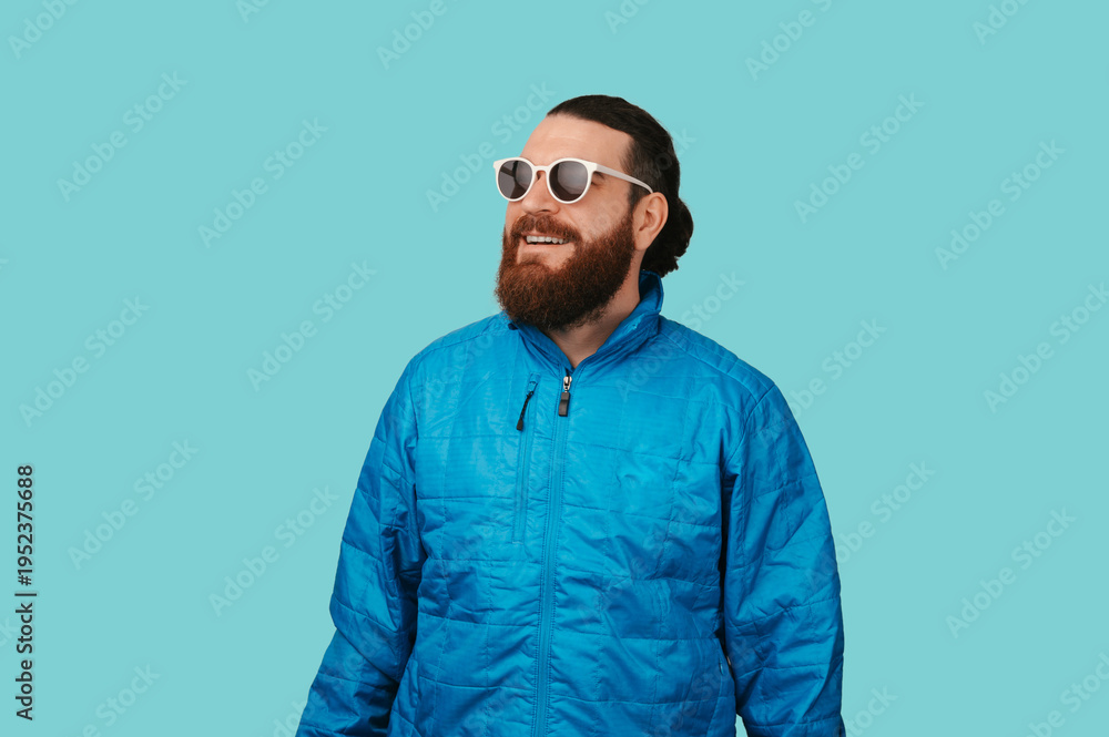 Fototapeta premium Smiling Caucasian Man Wearing Sunglasses And Blue Jacket Looking Upward With Relaxed Confident Vibe, Studio